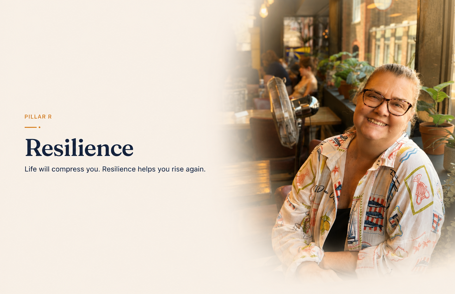 Jo-Dee Walmsley smiling warmly with arms crossed in a plant-filled coffee shop, sunlight coming through the window behind her.
